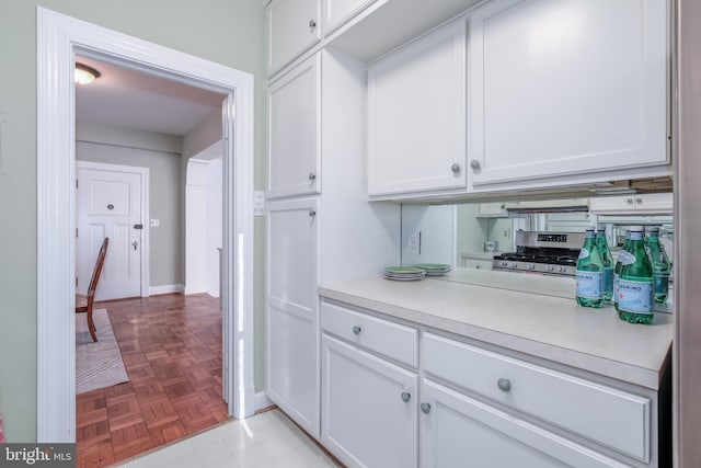 bar with white cabinetry, stainless steel gas stove, and light parquet flooring