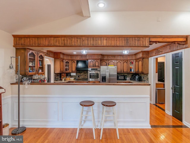 kitchen featuring decorative backsplash, kitchen peninsula, stainless steel appliances, vaulted ceiling, and light hardwood / wood-style flooring