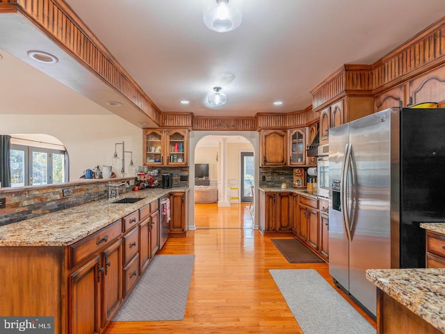 kitchen featuring sink, tasteful backsplash, light stone counters, light hardwood / wood-style floors, and appliances with stainless steel finishes