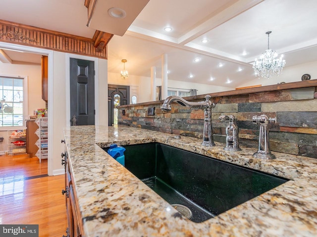 kitchen featuring light wood-type flooring, sink, pendant lighting, beam ceiling, and an inviting chandelier