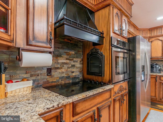 kitchen featuring decorative backsplash, stainless steel appliances, light stone counters, and premium range hood