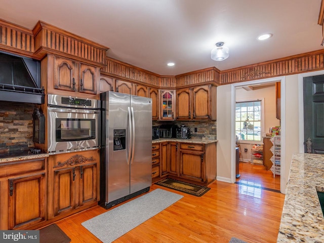 kitchen featuring light stone countertops, light wood-type flooring, stainless steel appliances, and tasteful backsplash