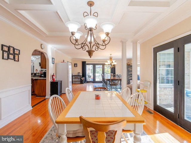 dining room featuring french doors, decorative columns, ornamental molding, a notable chandelier, and light hardwood / wood-style floors