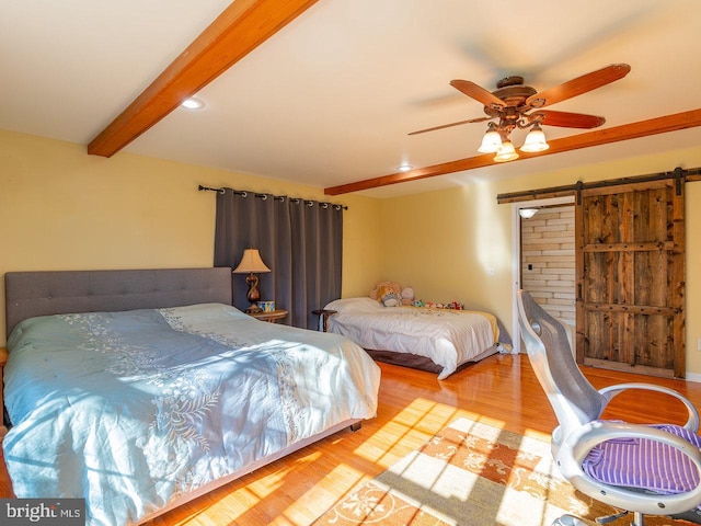 bedroom featuring beamed ceiling, ceiling fan, a barn door, and light wood-type flooring