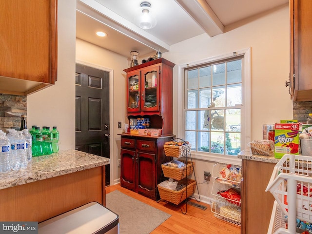 kitchen with beam ceiling, backsplash, light hardwood / wood-style flooring, and light stone counters