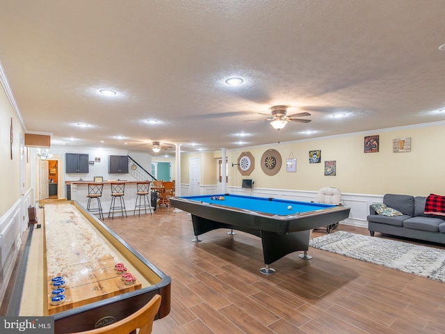 recreation room with pool table, bar area, wood-type flooring, a textured ceiling, and ornamental molding