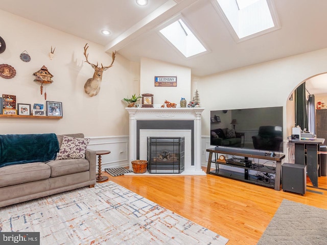 living room with a tile fireplace, hardwood / wood-style floors, and vaulted ceiling with skylight