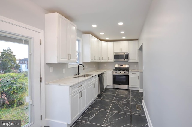 kitchen with light stone countertops, white cabinetry, sink, and stainless steel appliances