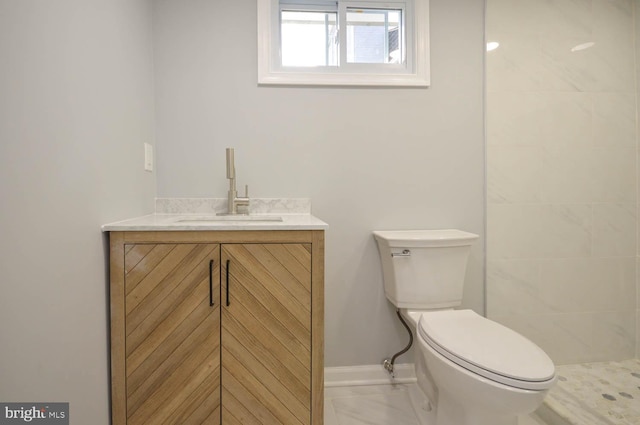 bathroom with a tile shower, vanity, and toilet