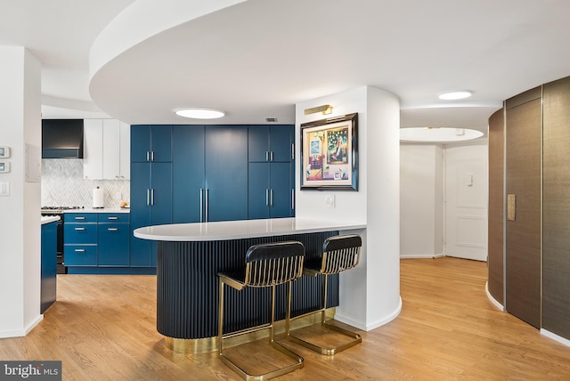 kitchen featuring a breakfast bar, wall chimney range hood, light wood-type flooring, blue cabinetry, and kitchen peninsula