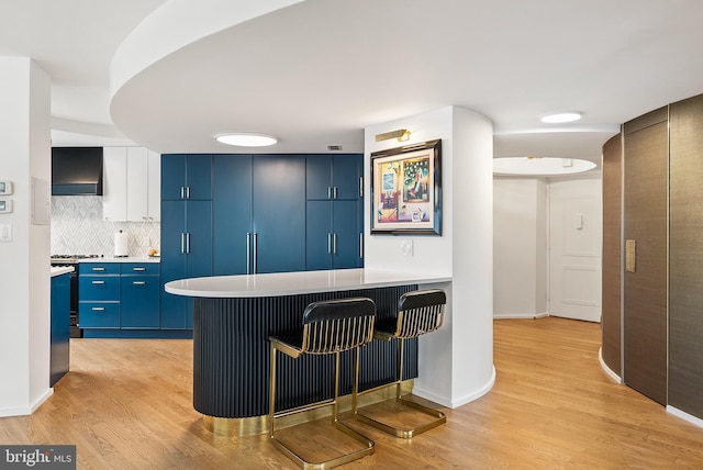 2510 Virginia Ave NW Unit 1104-N, Washington, DC 20037 - kitchen with blue cabinetry, light wood finished floors, wall chimney range hood, and a peninsula