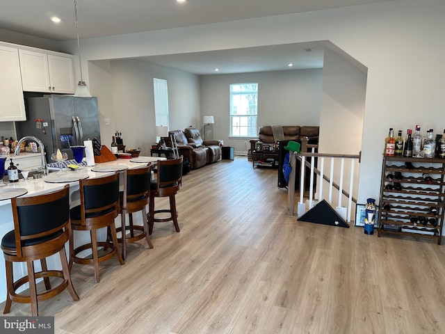 kitchen featuring a kitchen breakfast bar, sink, stainless steel fridge, light wood-type flooring, and white cabinetry