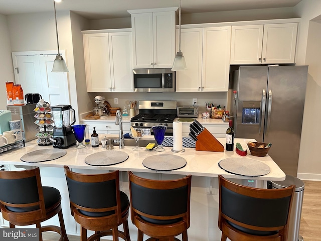 kitchen featuring sink, light hardwood / wood-style floors, decorative light fixtures, white cabinets, and appliances with stainless steel finishes