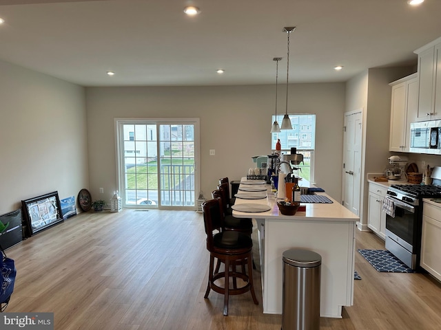 kitchen with stainless steel appliances, light hardwood / wood-style floors, decorative light fixtures, a center island with sink, and white cabinets