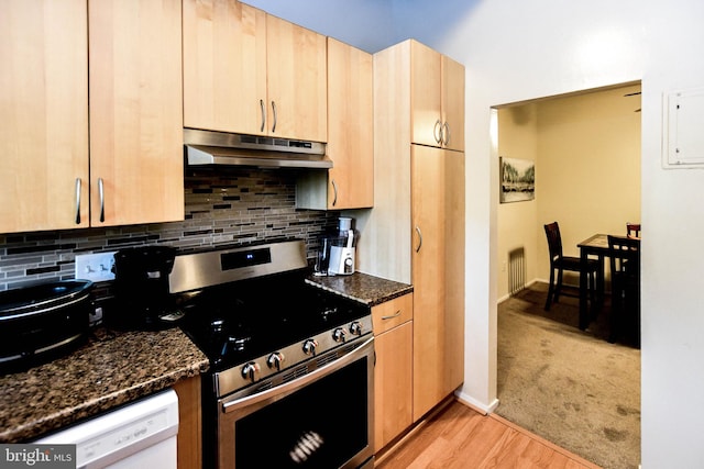 kitchen featuring stainless steel range, light brown cabinets, tasteful backsplash, dark stone countertops, and light wood-type flooring