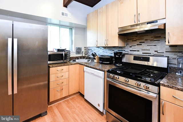 kitchen featuring light brown cabinets, sink, dark stone countertops, light wood-type flooring, and appliances with stainless steel finishes