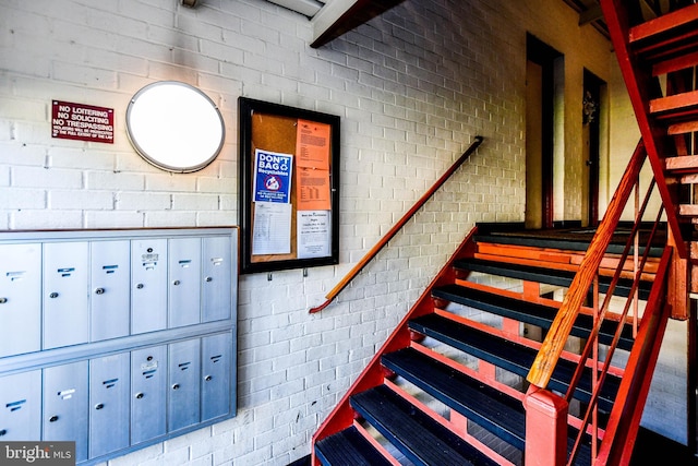 stairway featuring brick wall and a mail area