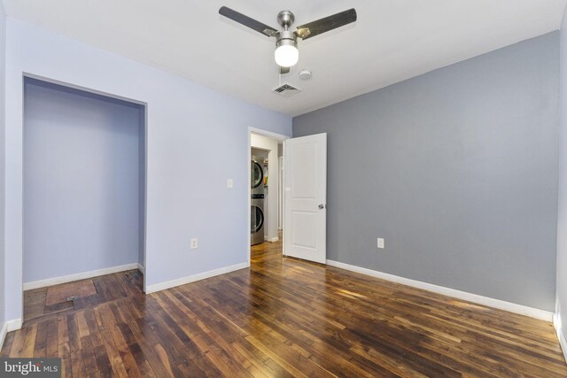 unfurnished bedroom featuring stacked washing machine and dryer, wood finished floors, baseboards, and a ceiling fan