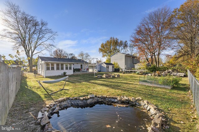 back of property with a vegetable garden, a garden pond, and an outdoor structure