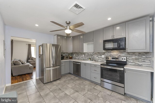 kitchen featuring gray cabinetry, appliances with stainless steel finishes, a sink, decorative backsplash, and recessed lighting