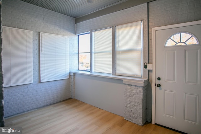 foyer entrance with light hardwood / wood-style floors and brick wall