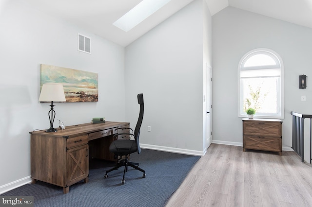 home office with high vaulted ceiling, a skylight, and light hardwood / wood-style flooring