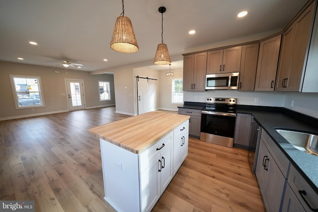 kitchen with a center island, light hardwood / wood-style flooring, a barn door, appliances with stainless steel finishes, and butcher block counters