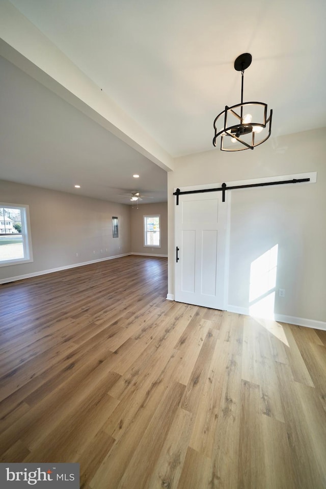 interior space featuring a barn door, light hardwood / wood-style flooring, and ceiling fan with notable chandelier