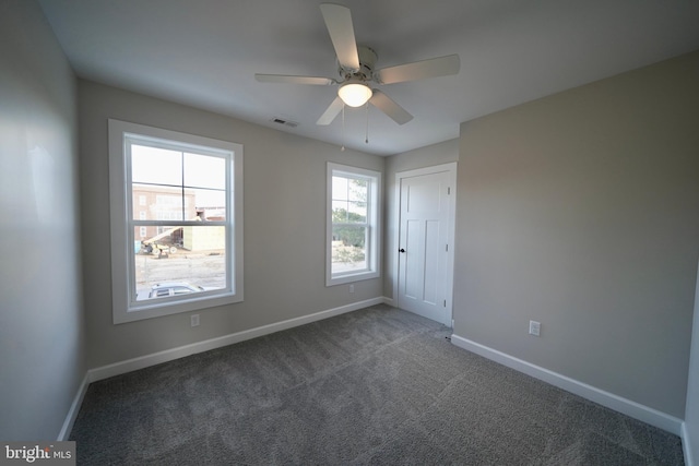 spare room featuring ceiling fan, plenty of natural light, and dark colored carpet