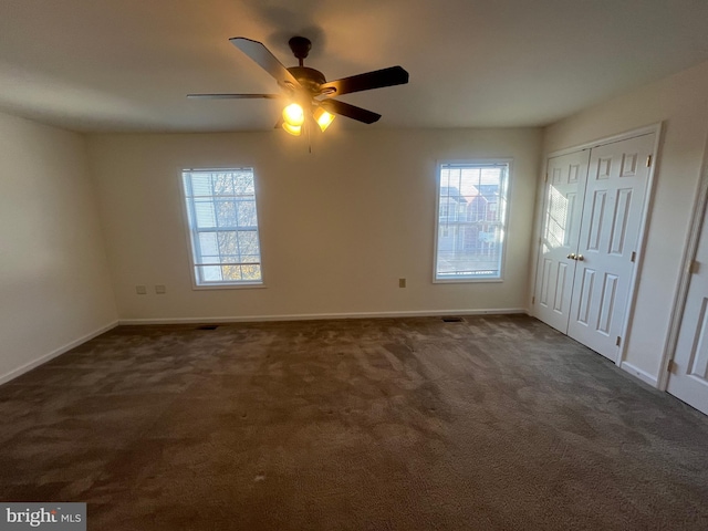 unfurnished bedroom featuring dark colored carpet, multiple windows, and ceiling fan