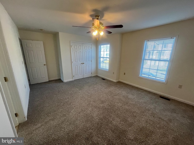 unfurnished bedroom featuring dark colored carpet, ceiling fan, and multiple windows