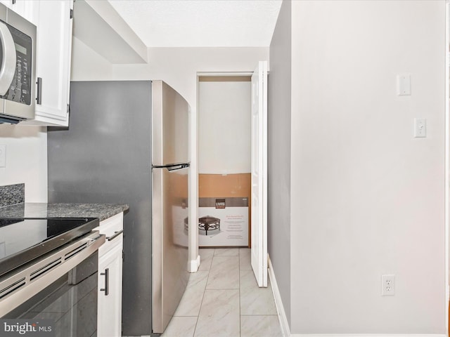 kitchen with dark stone counters, white cabinetry, stainless steel appliances, and a textured ceiling