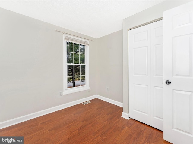 unfurnished bedroom with a textured ceiling, a closet, and dark hardwood / wood-style floors