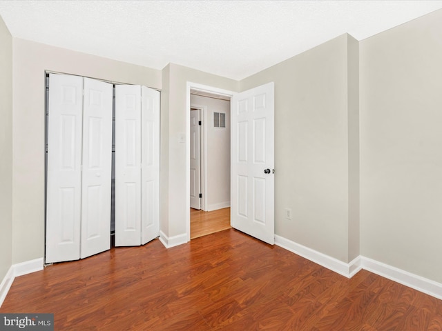 unfurnished bedroom with wood-type flooring, a textured ceiling, and a closet