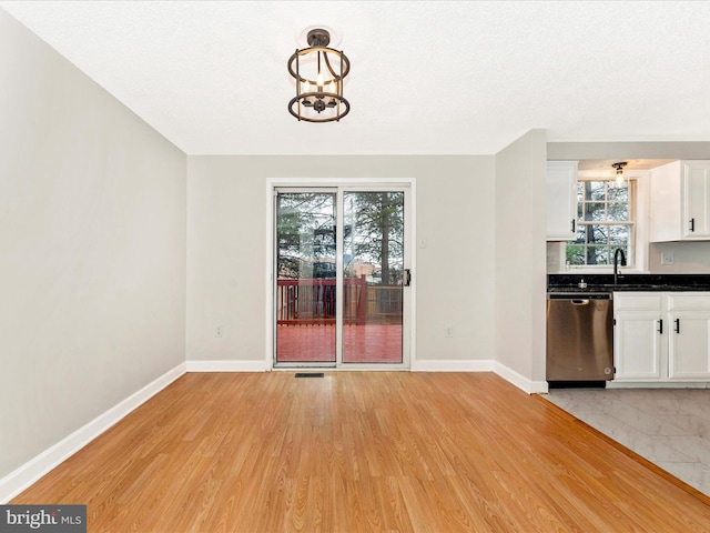 unfurnished dining area featuring light hardwood / wood-style floors, a textured ceiling, and an inviting chandelier