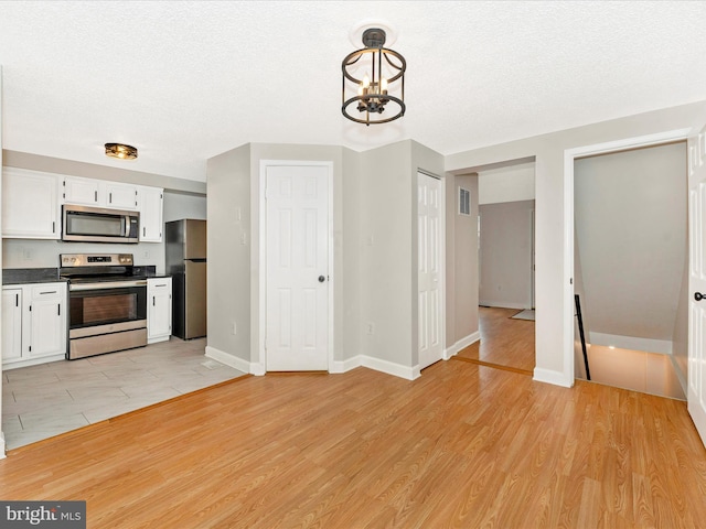 kitchen with white cabinetry, stainless steel appliances, a chandelier, decorative light fixtures, and light wood-type flooring