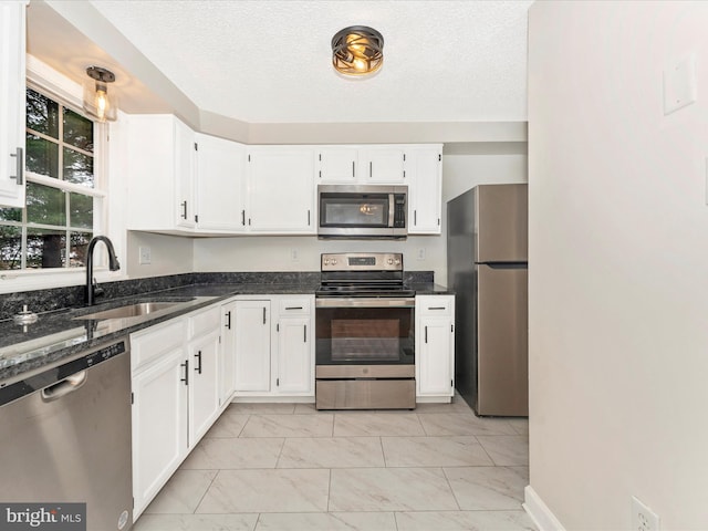 kitchen featuring dark stone counters, white cabinets, sink, a textured ceiling, and stainless steel appliances