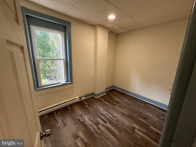 empty room with a drop ceiling, dark hardwood / wood-style floors, and baseboard heating