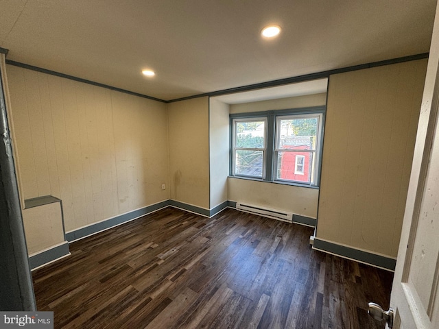 empty room with baseboard heating, crown molding, wooden walls, and dark wood-type flooring