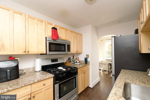 kitchen with appliances with stainless steel finishes, dark hardwood / wood-style flooring, light stone counters, sink, and light brown cabinets