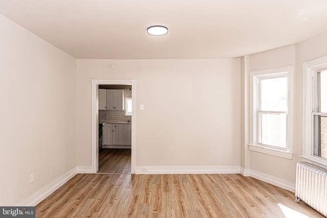 unfurnished room featuring radiator heating unit and light hardwood / wood-style floors