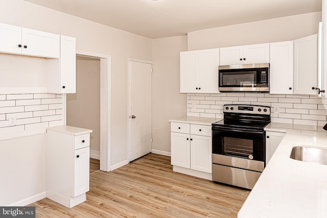 kitchen with tasteful backsplash, white cabinetry, light hardwood / wood-style floors, and appliances with stainless steel finishes