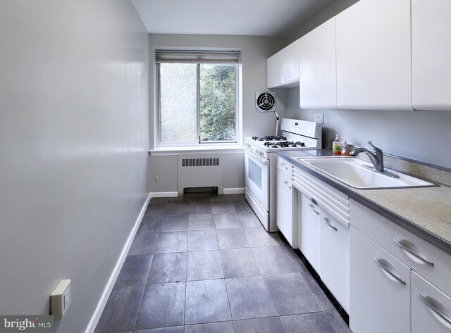 kitchen with dark tile patterned flooring, radiator heating unit, sink, white gas range oven, and white cabinetry