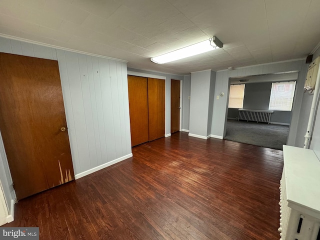 empty room with dark hardwood / wood-style floors, radiator, and wooden walls