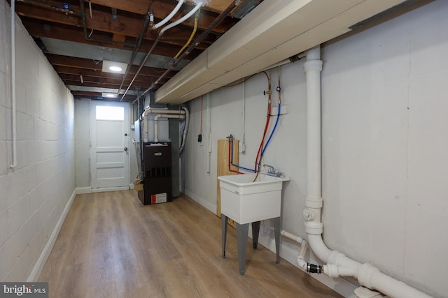 basement featuring light wood-type flooring, sink, and heating unit