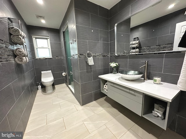 bathroom with tile patterned flooring, toilet, vanity, a shower with shower door, and tile walls