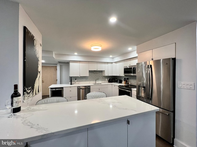 kitchen featuring a kitchen breakfast bar, kitchen peninsula, decorative backsplash, appliances with stainless steel finishes, and white cabinetry