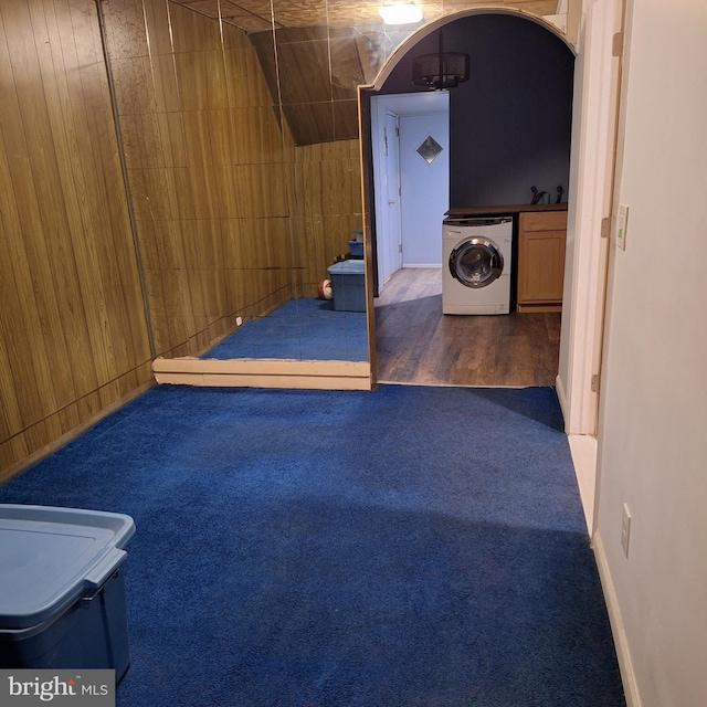 basement featuring washer / clothes dryer, wooden walls, and dark hardwood / wood-style flooring