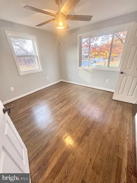 spare room featuring ceiling fan, a healthy amount of sunlight, and dark hardwood / wood-style flooring