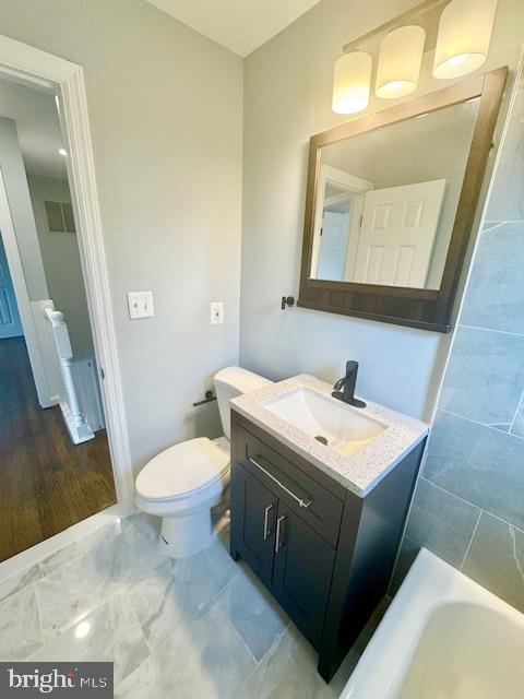 bathroom with a tub to relax in, vanity, wood-type flooring, and toilet